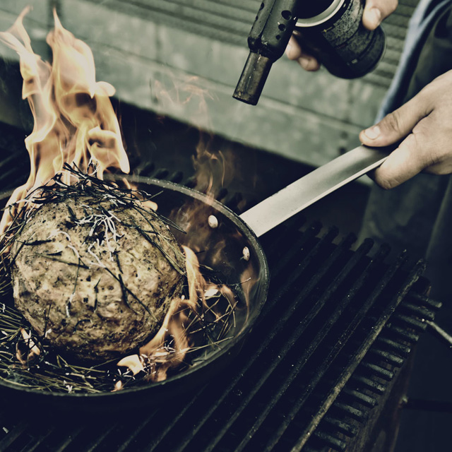 Chef making a grilled dish in a frying pan.