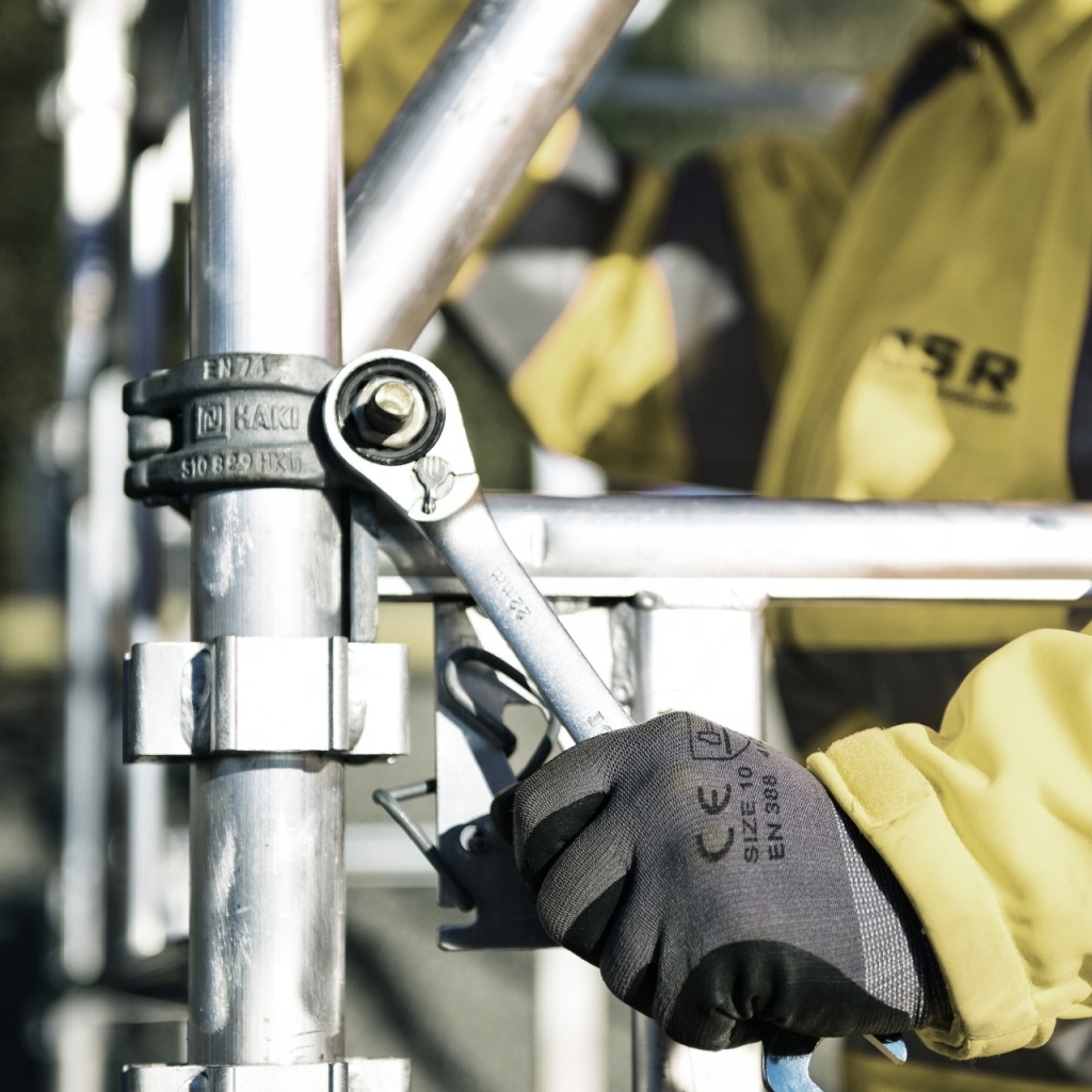 A worker screwing together a scaffolding.