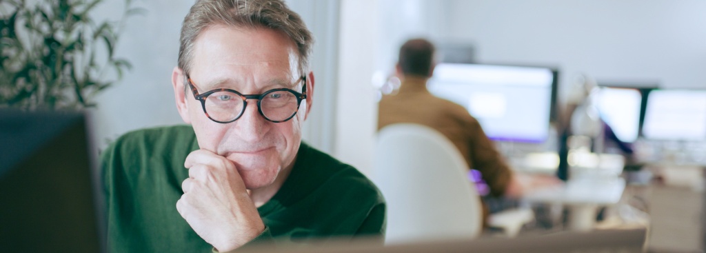a man with glasses smiling in front of his computer